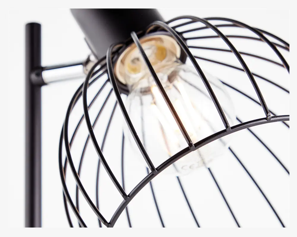 Nærbillede af en lampe med et sort metalbur-design, der omgiver en klar, synlig pære. Buret består af jævnt fordelte, buede metalstænger, hvilket giver et industrielt og moderne udtryk. Pæren er en standard skruepære med synlig glødetråd, og lampen er monteret på en lodret sort stang.
