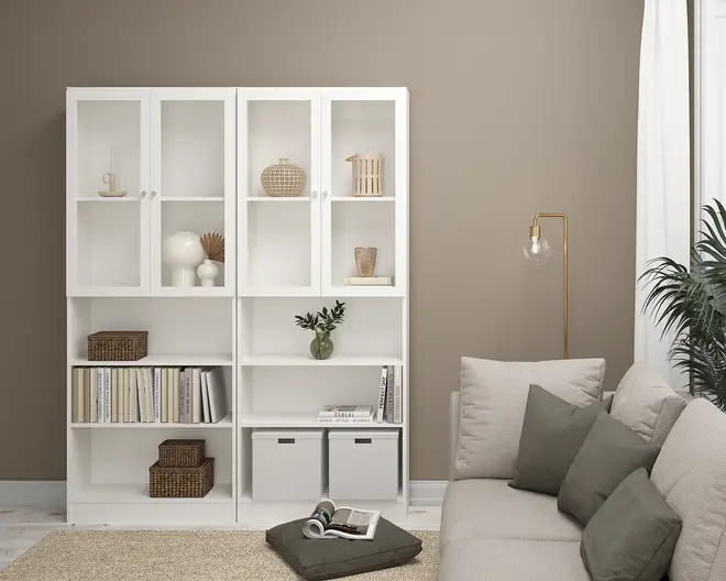 Høj, hvid reol med en kombination af åbne og glaslåger. Hylderne er dekoreret med flettede kurve, keramiske vaser, bøger og opbevaringskasser. Reolen har et rent, moderne design med lige linjer og mat finish, velegnet til nutidige indretninger.