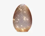 Dekorativt lys formet som et æg med en tekstureret glasoverflade i spiral-mønster. Glasset har en let ravfarvet tone og indeholder små, varme hvide LED-lys indeni, som giver en blød, glødende effekt. Basen er flad, så den står stabilt på overflader.