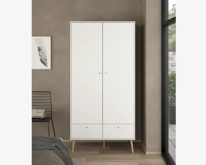 Høj, fritstående skab med minimalistisk design, to store låger med små runde greb og to rummelige skuffer nederst. Skabet er mat hvidt og står på fire skråtstillede ben i lyst træ, hvilket giver et moderne og rent udtryk.