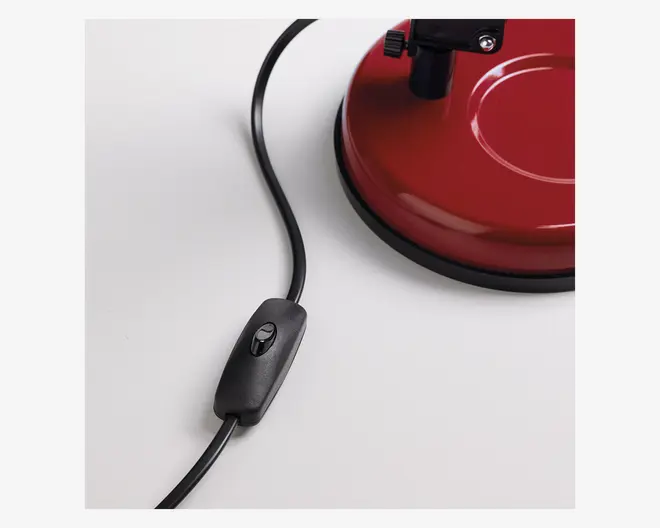 Nærbillede af en sort ledningsafbryder monteret på en ledning, ved siden af en rund, rød metalbase med sort gummikant. Basen har en blank overflade og en cirkulær fordybning, og der er monteret en metalbeslag ovenpå.