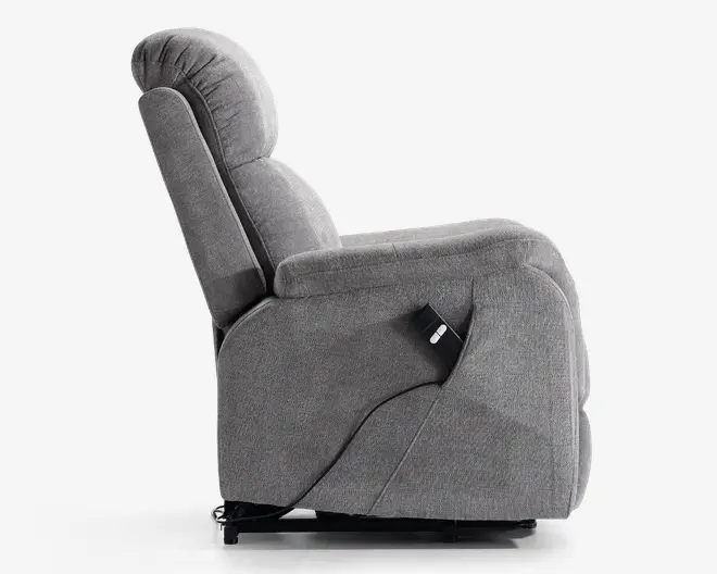 Sidebillede af en grå polstret reclinerstol med en blød, polstret ryg og sæde for ekstra komfort. Stolen har en indbygget fjernbetjening fastgjort på siden, hvilket viser, at den er elektrisk justerbar. Armlænene er brede og polstrede, og det samlede design er moderne og funktionelt, velegnet til afslapning.