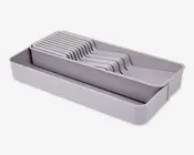 Rektangulær, lysegrå plastikbakke med flere skrå rum, der er designet til at holde bestik eller køkkenredskaber adskilt. Bakken har et trappet, pladsbesparende design, som gør det nemt at sortere og få adgang til de enkelte dele. Glatte overflader og afrundede hjørner gør den let at rengøre.