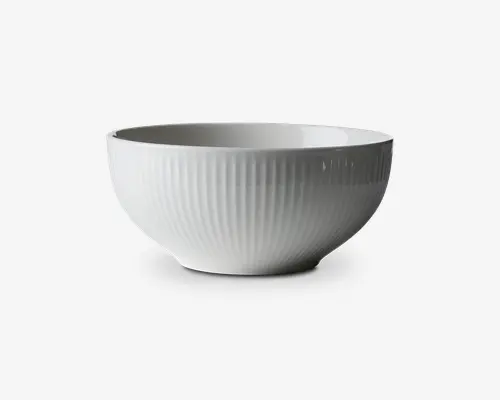En hvid skål med en diskret lodret rillet tekstur på ydersiden. Skålen har en glat, blank finish og en blødt afrundet form med en bred åbning og en lidt smallere bund. Designet er minimalistisk og elegant, velegnet til både daglig brug og særlige lejligheder.