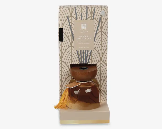Fragranceflaske i ravfarvet glas med rund trælåg og gylden kvast, præsenteret i en høj mønstret gaveæske med en beige etiket med teksten Amber & Sandalwood.