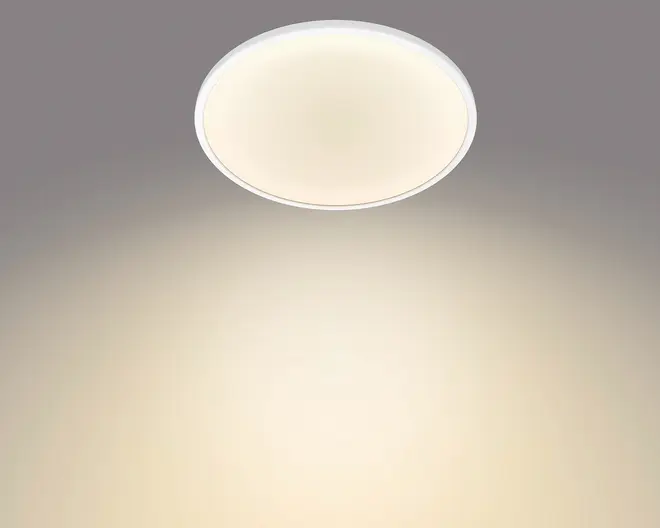 Rund loftlampe til plan montering med hvid kant og blødt varmt lys, vist tændt mod et gråt loft.