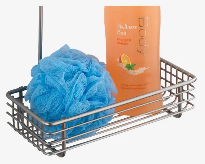 En rektangulær brusekurv i metal med blank sølvfinish og et lodret håndtag på den ene side. I kurven ligger en lys blå mesh-badesvamp og en orange flaske med bodywash mærket 'Wellness Bad Orange & Melisse.' Flasken har et billede af en appelsinskive og mynteblade på forsiden.