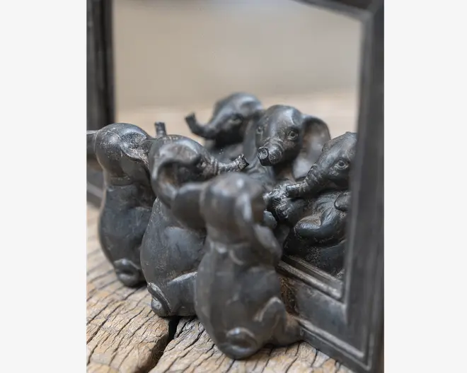Små mørke dyrefigurer med lange snuder og hængeører samlet foran et spejl, så de gentages i refleksionen på en slidt træoverflade.