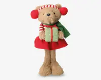 En bamse med lysebrun pels iført en rød nederdel, et grønt tørklæde og rød-hvide stribede ørevarmere og hue. Bamsen holder en grøn gaveæske med rød bånd. Den ene arm har en rød-hvid stribet ærme, hvilket understreger det festlige juletema.