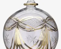 Klar glaskugle med indviklede guldfarvede båndmønstre og indgraverede stjernemotiver. Overfladen har både glatte og teksturerede områder, hvor gulddetaljer fremhæver de dekorative elementer. Toppen har en lille løkke til ophæng, også med gulddetalje.