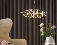 Et moderne pendellampe-armatur med en cirkulær metalramme, der har et indviklet design af grene og blade. Lampen har flere synlige pærer, som giver en varm belysning. Metallet har en poleret, reflekterende finish, hvilket tilføjer elegance og et naturinspireret udtryk til rummet.