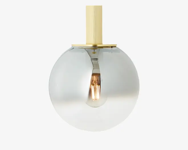 Et moderne lysarmatur med en rund, klar glaskuppel og en synlig glødepære indeni. Armaturet har en stang og monteringsplade i messing- eller guldfarvet metal, hvilket giver et stilrent og nutidigt udtryk.