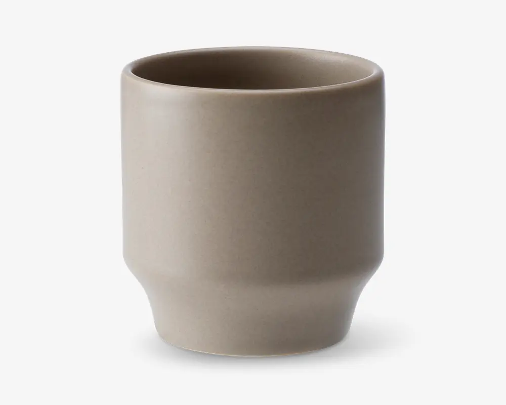 En minimalistisk, cylindrisk kop med mat taupe-finish. Koppen har lige sider, der let smalner ind mod bunden og danner en diskret fod. Randen er glat og let afrundet, og overfladen er uden dekoration, hvilket giver et moderne og enkelt udtryk.