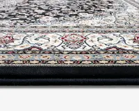 Nærbillede af et tykt, blødt tæppe med en detaljeret og udsmykket kant, der viser indviklede blomster- og snirklemønstre i nuancer af creme, rød, blå og sort. Tæppet har en tæt luv, hvilket giver en blød og polstret overflade. Farverne og designet antyder en klassisk, elegant stil, der passer til traditionelle indretninger.