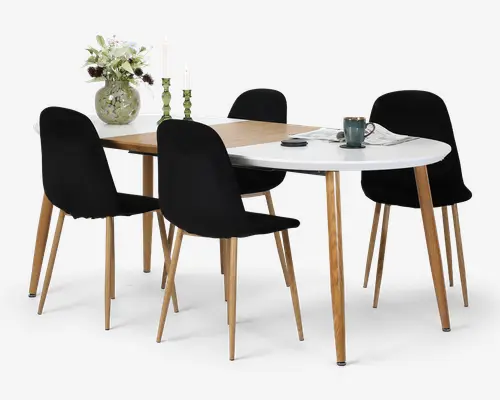 Moderne spisebordssæt med todelt bordplade i træ og hvidt med afrundede kanter, omgivet af fire sorte stole med lyse træben; vase med blomster, lys og servise på bordet.