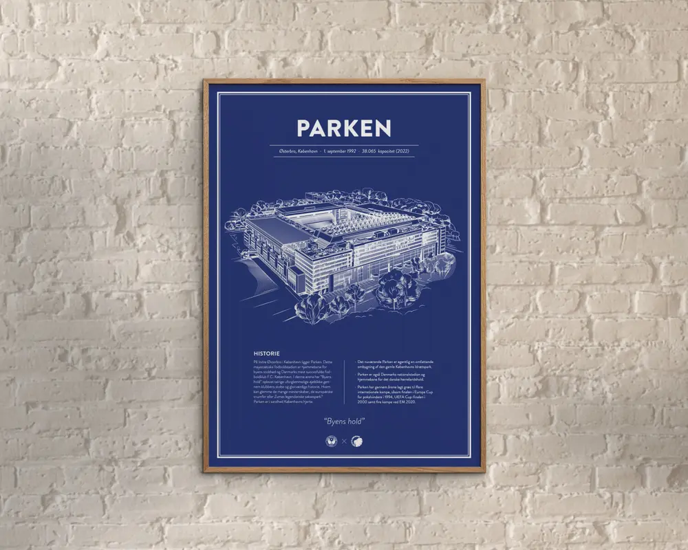 En indrammet plakat med en blueprint-lignende illustration af et stadion, tegnet med detaljerede hvide linjer på en dyb blå baggrund. Øverst på plakaten står 'PARKEN' med store hvide bogstaver, og derunder er der yderligere information om sted og datoer. Nederst er der tekstblokke og et citat, alt sammen i hvidt, med et rent og moderne layout. Rammen er slank og i lyst træ, og plakaten hænger på en lys murstensvæg.
