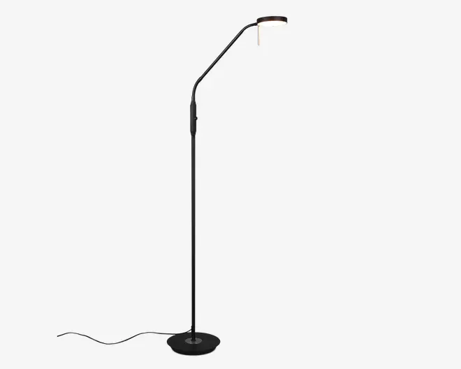 Høj, slank standerlampe med mat sort finish og en rund, stabil fod. Lampen har en justerbar arm med flere led, hvilket giver fleksibel placering af lyset. Lampeskærmen er rund og udsender et blødt, varmt lys, ideelt til læsning eller arbejdsbelysning. Strømledningen går ud fra bunden for nem tilslutning.