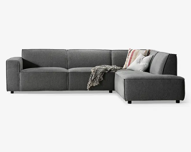 Moderne hjørnesofa med højrevendt chaiselong, betrukket med mørkegråt stof. Sofaen har brede, firkantede armlæn og dybe, bløde sædehynder for ekstra komfort. Der medfølger to pyntepuder—en med stribet mønster og en ensfarvet hvid—samt et tekstureret tæppe, der er lagt over chaiselongen. Sofaen har et lavt design og står på korte, solide ben.