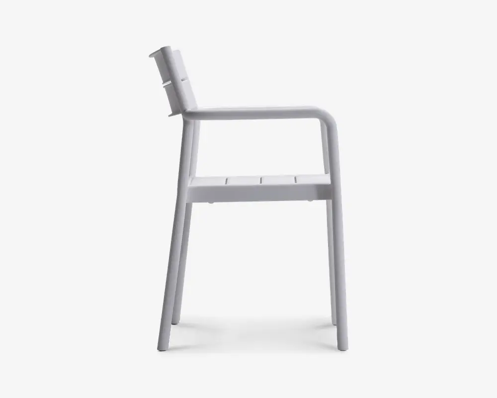 Sideprofil af en stol med minimalistisk design, lige ryglæn, flad sæde med slidser til dræning og integrerede armlæn. Stolen er fremstillet i ét materiale, sandsynligvis metal eller plastik, og har en glat, mat overflade. Benene er let skråtstillede for stabilitet.