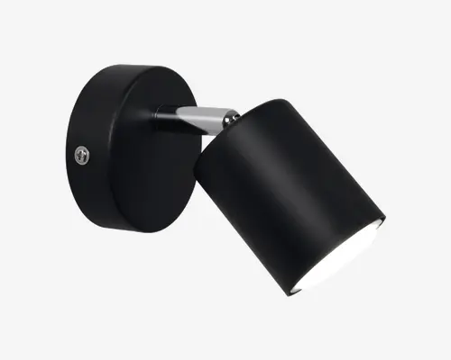 Væghængt lampe i mat sort med cylinderformet, justerbart lampehoved. Lampen har en rund base med en synlig skrue til montering og en kort metalarm, der forbinder basen med lampehovedet. Lampehovedet kan vinkles, så lyset kan rettes efter behov, hvilket gør den velegnet til arbejds- eller stemningsbelysning.