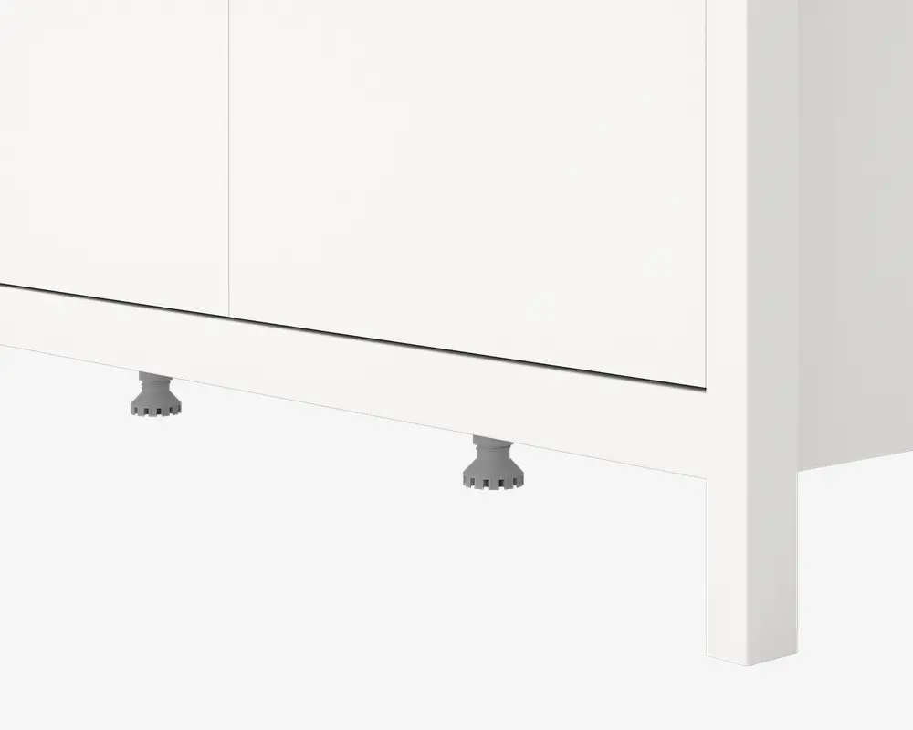 Nærbillede af den nederste del af et hvidt skab med glatte, flade paneler og et minimalistisk design. Skabet står på justerbare grå plastikben, som delvist kan ses under soklen. Overfladen er mat, og kanterne er lige og rene, hvilket giver et moderne udtryk.