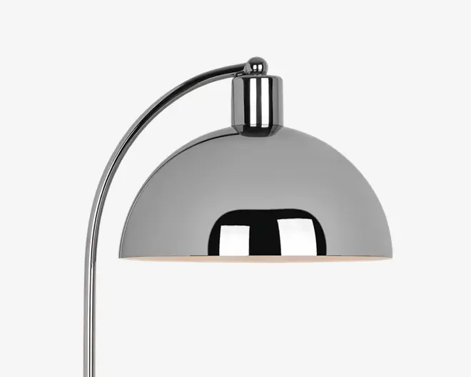 Nærbillede af en moderne lampe med blank kromfinish. Lampen har en kuppelformet skærm og en buet arm, hvilket giver et stilrent og moderne udtryk. Den reflekterende overflade på skærmen tilføjer et elegant præg, og den åbne bund giver direkte lys nedad.
