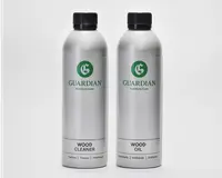 To høje, cylindriske sølvfarvede flasker med sorte skruelåg. Flasken til venstre er mærket 'Wood Cleaner', og flasken til højre er mærket 'Wood Oil'. Begge flasker har et grønt 'G'-logo og mærket 'Guardian Furniture Care'. Etiketterne er enkle og moderne med tydelig sort tekst på hvid baggrund nederst på hver flaske. Flaskerne ser ud til at være lavet af metal og er designet til nem hældning og opbevaring.