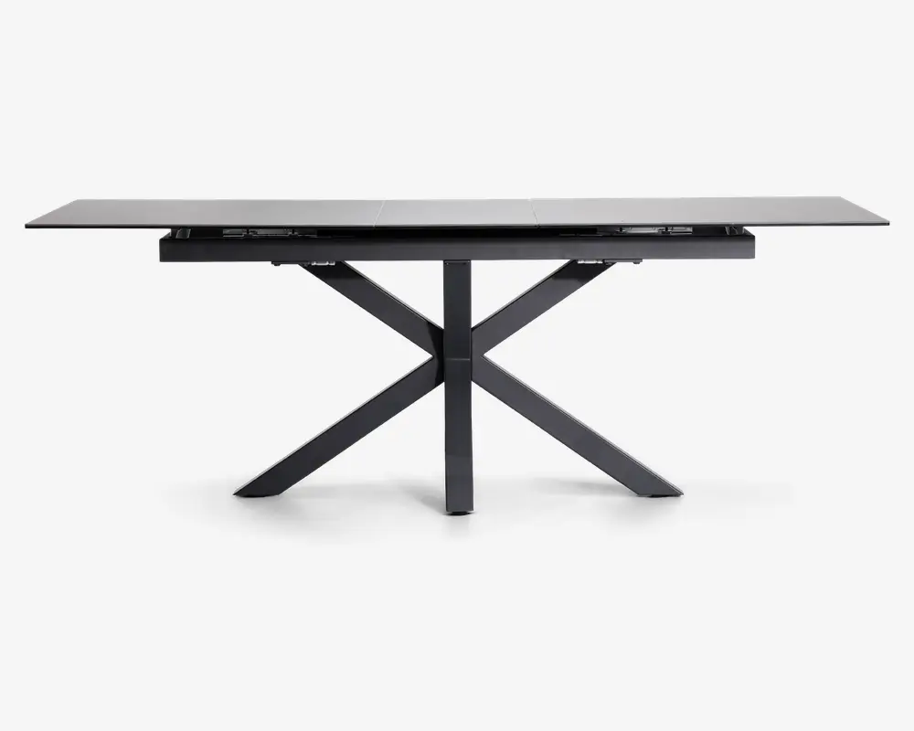 Rektangulært bord med en elegant, mat sort finish. Bordpladen ser ud til at være lavet af et solidt materiale og understøttes af et karakteristisk krydset benstel, som giver både stabilitet og et moderne udtryk. Bordet har rene linjer og et minimalistisk design, der passer til moderne indretning.