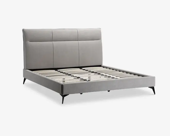 Moderne sengeramme med et lysegråt polstret hovedgærde, der har tre store rektangulære paneler. Rammen har en lav profil med matchende gråt stof på sider og fodende. Sengen har jævnt fordelte lameller i træ til madrasstøtte og står på slanke, skrå sorte ben.