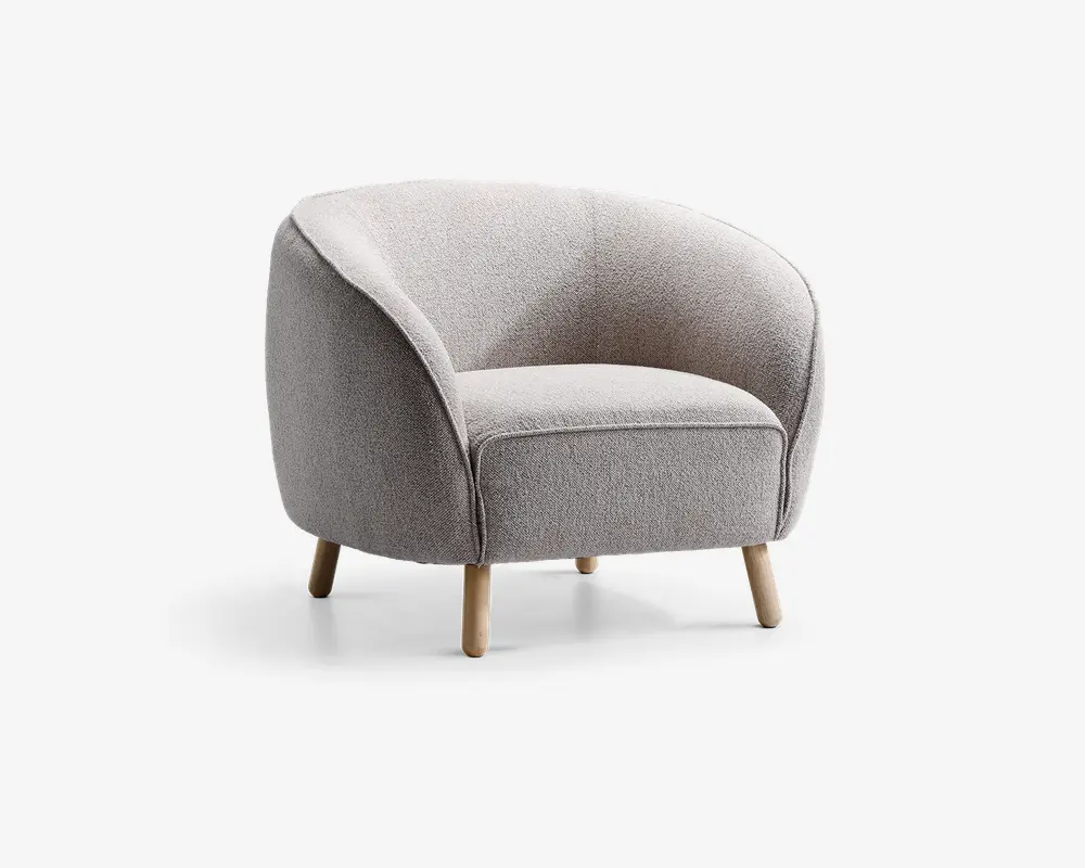 En moderne lænestol med rund ryg og sider, polstret med lysegråt tekstureret stof. Sædepuden er tyk og blød for ekstra komfort. Stolen står på fire korte, skråtstillede træben med naturfinish, hvilket giver et moderne og hyggeligt udtryk.