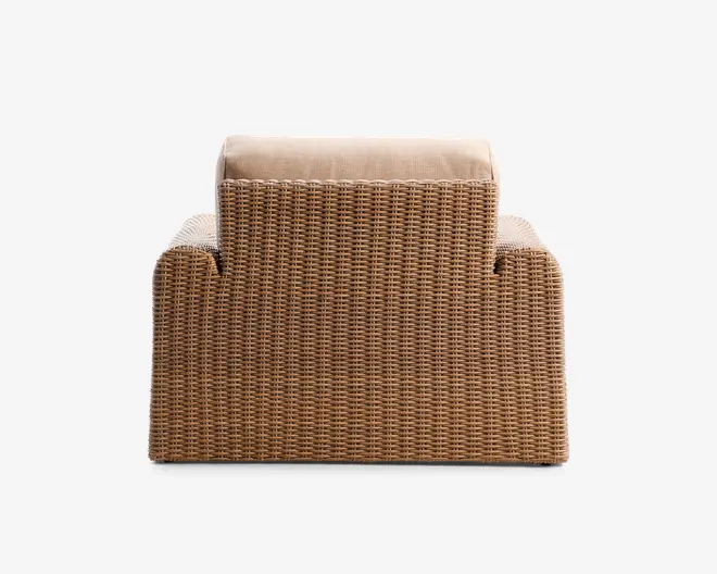 Lænestol med flettet rattan-lignende ydre i en naturlig brun farve, designet med en firkantet, moderne form, brede armlæn og en tyk, lysebeige pude på ryglænet for ekstra komfort.
