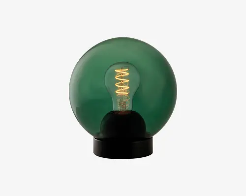 En dekorativ bordlampe med en rund, mørkegrøn glasafskærmning, der omslutter en synlig glødepære. Pæren udsender et varmt, stemningsfuldt lys og står på en elegant, sort cirkulær fod. Lampen har et moderne, minimalistisk design med et retropræg på grund af den synlige spiralformede glødetråd.