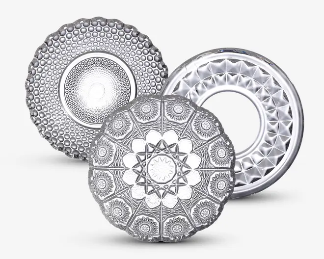 Sæt med tre klare glasfade, hver med et unikt præget mønster. Den første tallerken har en hævet bobletekstur i koncentriske cirkler. Den anden tallerken viser et geometrisk stjernemønster med indviklede blomster- og diamantformer. Den tredje tallerken er ringformet med facetslebet diamantmønster langs kanten og et åbent center. Alle fade har en reflekterende, blank overflade.