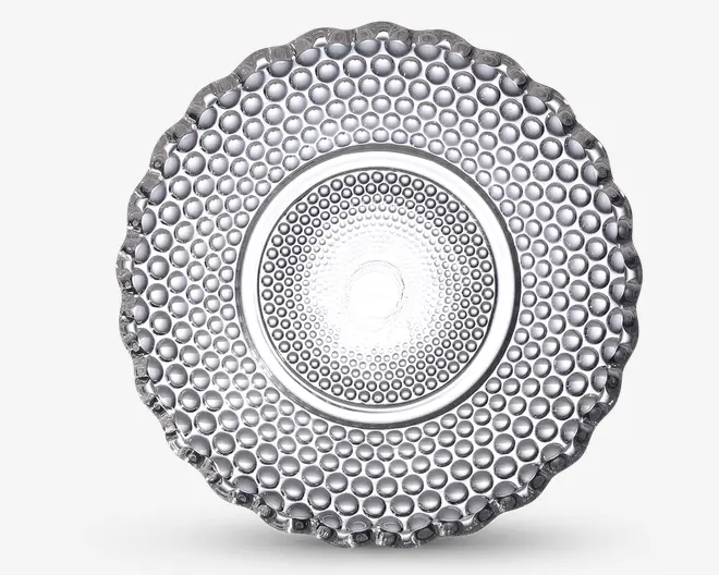 Klar glas-tallerken med en tekstureret overflade, der har et mønster af hævede, runde bobler i koncentriske cirkler. Kanten er bølget, hvilket giver et dekorativt udtryk. Tallerkenen har et glat område i midten omgivet af boblemønsteret, hvilket giver et moderne og elegant udseende.