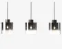 Sæt med tre pendellamper med cylindriske glasskærme, der har en farveovergang fra klar i bunden til røgfarvet sort i toppen. Hver lampe har en synlig glødepære indeni og hænger i en sort ledning og fatning, hvilket giver et moderne og elegant udtryk.