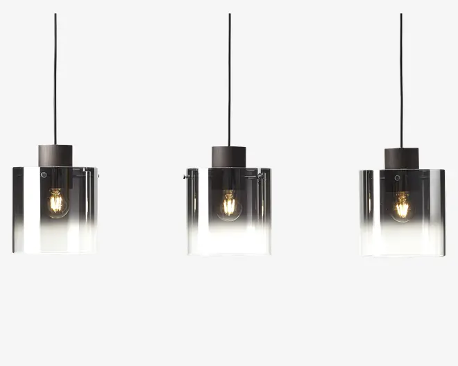 Sæt med tre pendellamper med cylindriske glasskærme, der har en farveovergang fra klar i bunden til røgfarvet sort i toppen. Hver lampe har en synlig glødepære indeni og hænger i en sort ledning og fatning, hvilket giver et moderne og elegant udtryk.