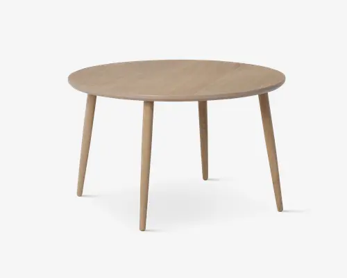 Rundt bord med en glat, lys træfinish. Har fire let skrå, tilspidsede ben for stabilitet og et minimalistisk, moderne design. Overfladen er flad og rummelig, velegnet til spisning eller arbejde.