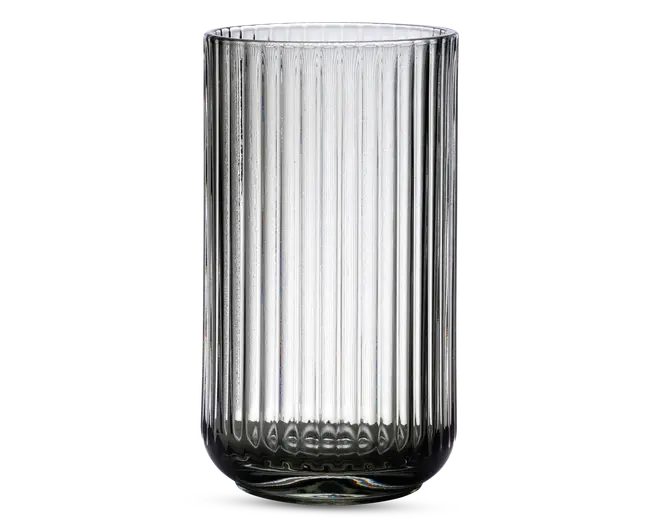 Høj, cylindrisk glas med en klar, gennemsigtig krop. Overfladen har lodrette rillede linjer, der løber fra top til bund og giver et tekstureret udseende. Glassets kant er glat, og bunden er let afrundet for stabilitet.