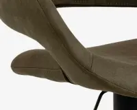 Nærbillede af en stol med buet, polstret ryglæn og sæde betrukket med olivengrønt ruskindslignende stof. Syningerne er synlige langs kanterne, og stolen har et moderne, ergonomisk design med en glat overflade.