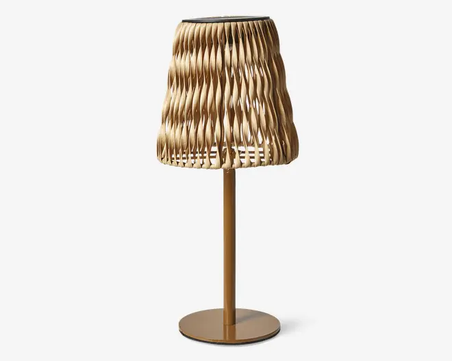 Bordlampe med en guldfarvet metalfod og en unik, skulpturel lampeskærm lavet af sammenflettede, bølgede strimler, der danner et tekstureret, åbent mønster. Skærmen lader lyset passere gennem åbningerne og kaster dekorative skygger. Designet er moderne og kunstnerisk, velegnet som et blikfang i nutidige indretninger.