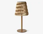 Bordlampe med en guldfarvet metalfod og en unik, skulpturel lampeskærm lavet af sammenflettede, bølgede strimler, der danner et tekstureret, åbent mønster. Skærmen lader lyset passere gennem åbningerne og kaster dekorative skygger. Designet er moderne og kunstnerisk, velegnet som et blikfang i nutidige indretninger.