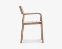 Sideprofil af en moderne stol med minimalistisk design, let tilbagelænet ryglæn, integrerede armlæn og fladt sæde med diskrete slidser for ventilation. Stolen er lavet af et glat, mat materiale i en lys beige farve og har blødt afrundede kanter for et moderne udtryk.