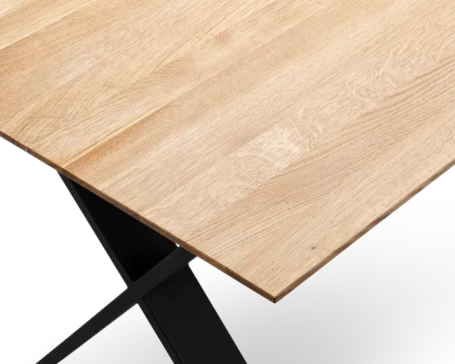 Nærbillede af en bordplade med en lys, naturlig træstruktur, der har en glat, flad overflade og let affaset kant. Bordpladen understøttes af en solid sort metalramme med krydsende ben, hvilket giver et moderne og minimalistisk udtryk.