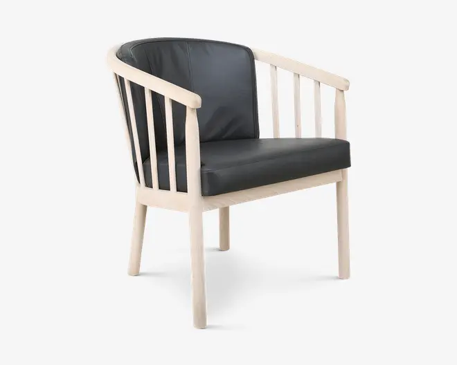 Stol med en lys træramme, der har lodrette lameller på ryg og sider, samt sæde og ryglæn polstret med glat sort læder. Designet kombinerer et moderne udtryk med klassiske elementer, og sædet ser velpolstret og komfortabelt ud.