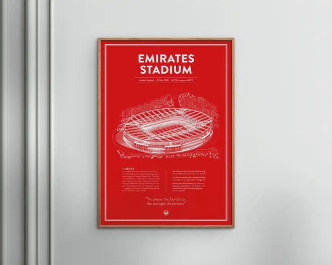 En indrammet plakat med en detaljeret hvid stregtegning af Emirates Stadium på en kraftig rød baggrund. Øverst på plakaten står stadionets navn med store, hvide bogstaver. Under illustrationen er der et afsnit med historisk information om stadionet samt et citat i mindre tekst. Plakaten har en tynd hvid kant og hænger på en lys væg.