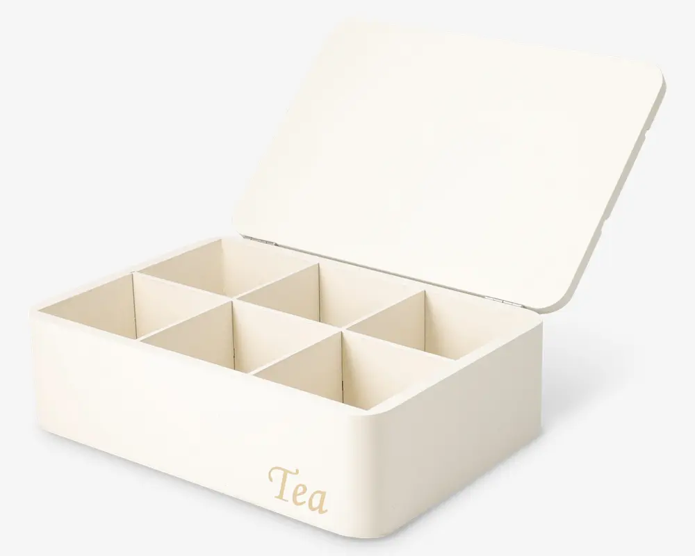 Rektangulær æske i cremefarve med hængslet låg, der har seks lige store rum indeni til organisering. Ordet 'Tea' er trykt med guldbogstaver på fronten. Æsken har glatte, afrundede kanter og et minimalistisk design.