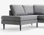 Lysegrå polstret hjørnesofa med bred chaiselong-lignende siddeplads, tre løse ryghynder og slanke sorte koniske ben i et rent, moderne design.