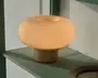 En lille bordlampe med en glat, rund skærm i ravfarvet glas og en kort cylindrisk fod, der udsender et varmt skær.