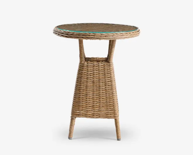 Rundt sidebord med flettet rattan-design i en naturlig lysebrun farve. Bordpladen er dækket af en klar glasplade, som giver ekstra holdbarhed og gør det nemt at rengøre. Basen har en let udvidet, konisk form med fire ben og en lille hylde under bordpladen til ekstra opbevaring eller dekoration. Udtrykket er let og passer både til indendørs og udendørs brug.