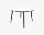 Et rundt bord med en glat, hvid bordplade og fire slanke, sorte metalben, der er let skråtstillede for stabilitet. Designet er minimalistisk og moderne med en tynd bordplade og et rent, enkelt udtryk.